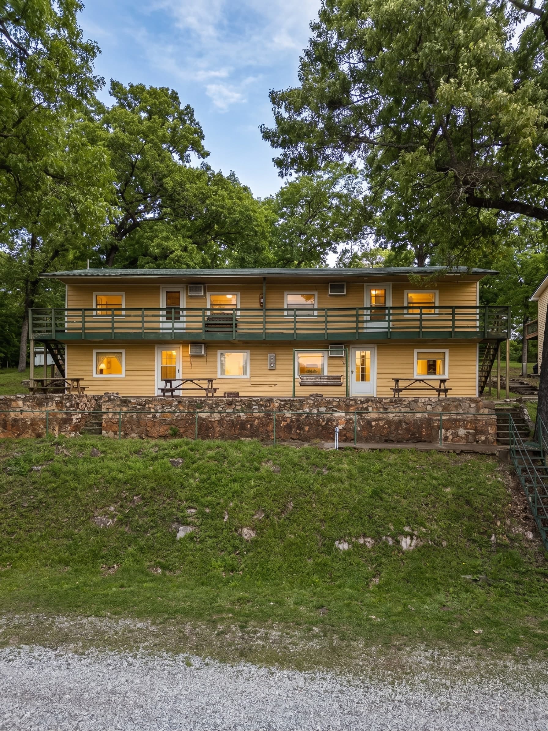Lakeside cabin exterior — two-story wood-sided building with upper and lower decks, stone retaining wall, and landscaped lawn
