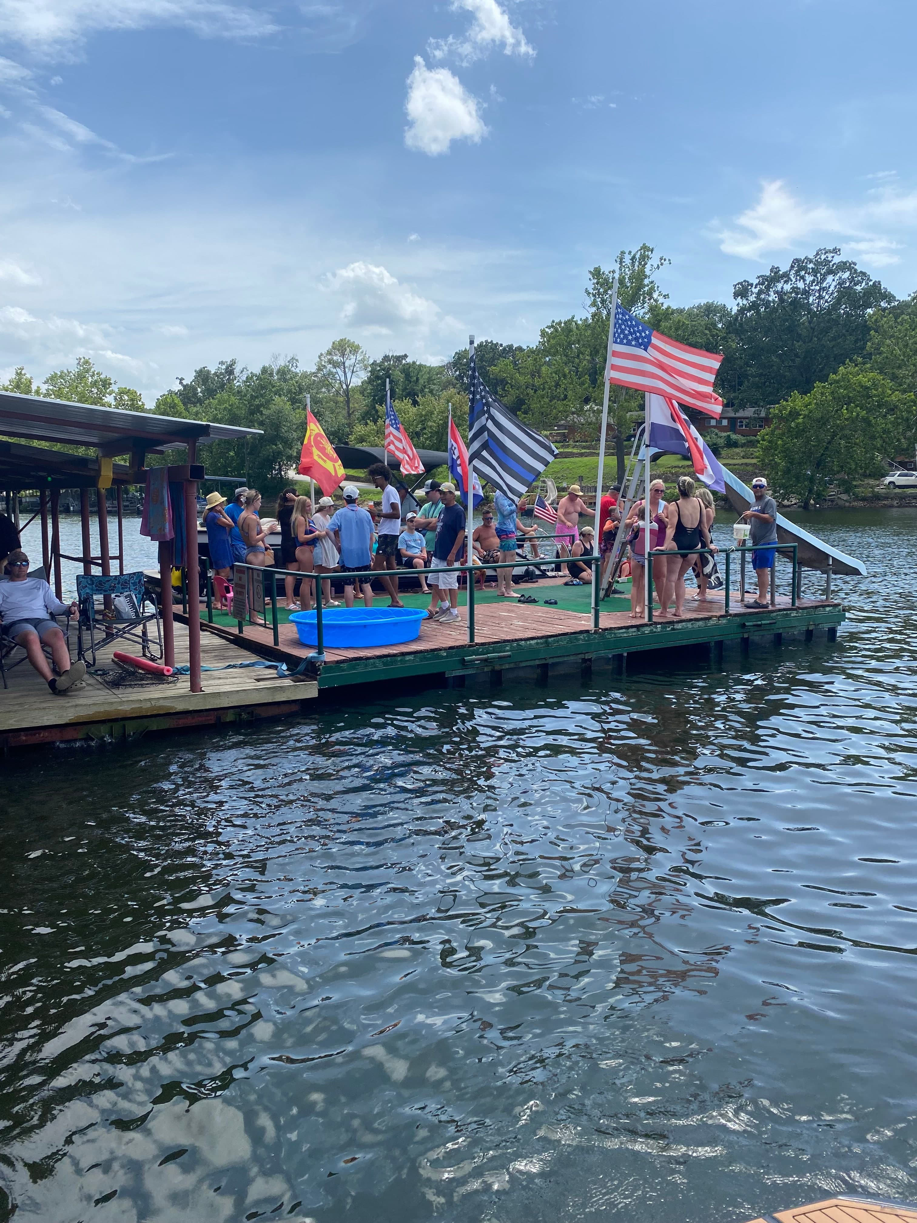 A full dock on a summer afternoon — chairs, flags, families, and the lake stretching out