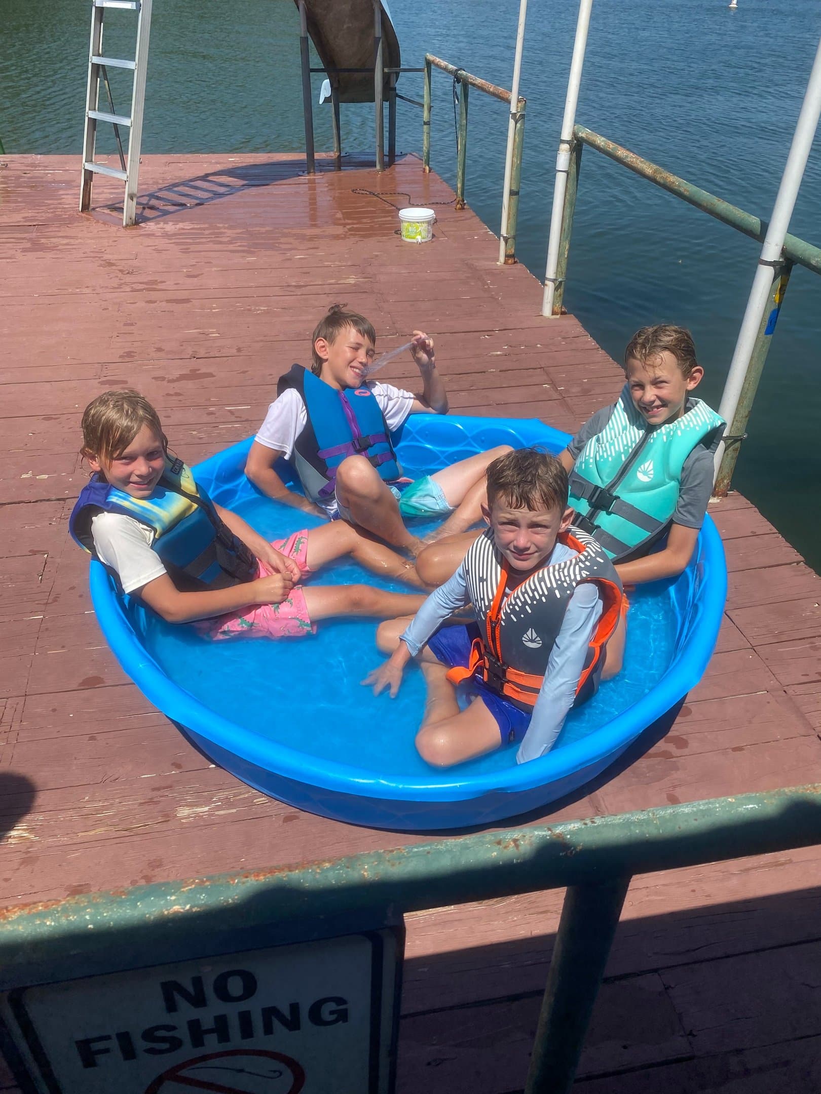 Four kids in life vests playing in an inflatable pool on the dock